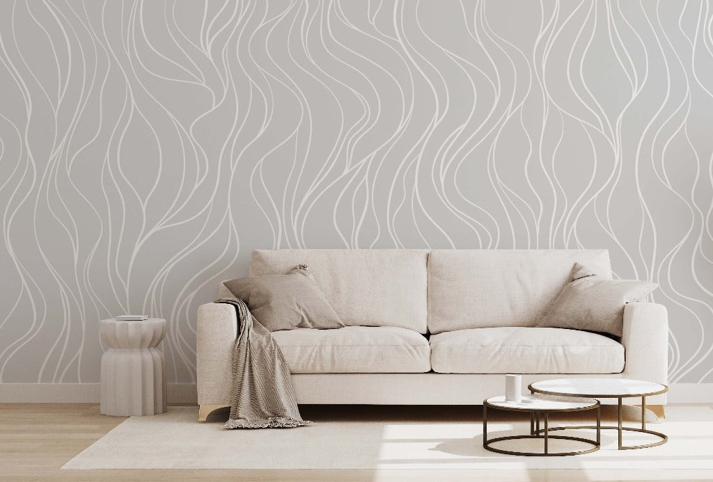 A minimalist bedroom with a beige sofa, adorned with matching cushions, against a Decor2Go Wallpaper Mural, featuring a small side table and a draped throw, highlighting a serene and stylish space.