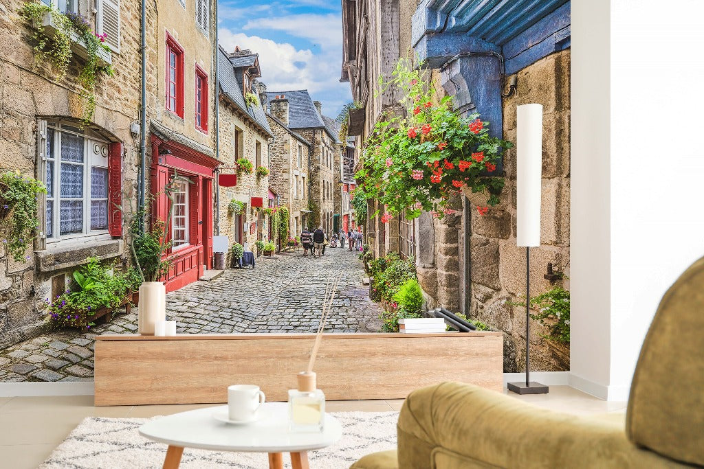 A cozy living room with a large Decor2Go Wallpaper Mural depicting an Antique European Alley, with charming, old street with cobblestones and colorful flowering balconies, viewed from a sofa with a small table in front.