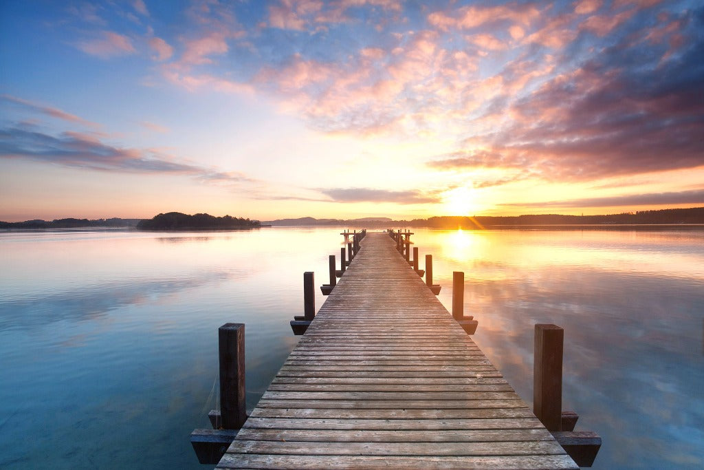 A tranquil sunset over a calm lake with a wooden pier extending towards the horizon under a vibrant sky painted with hues of orange, pink, and blue. (Docked Life Wallpaper Mural by Decor2Go Wallpaper Mural)