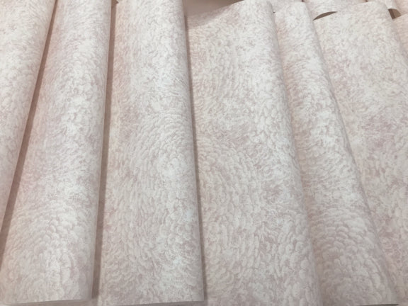 This close-up image features a design inspired by nature, showcasing the texture of off-white paper. With a delicate, swirling pattern reminiscent of York Wallcoverings' Floret Wallpaper Pink (60 SqFt), the paper is arranged in overlapping layers. This arrangement creates a sense of depth and repetition that emphasizes its sturdy material.