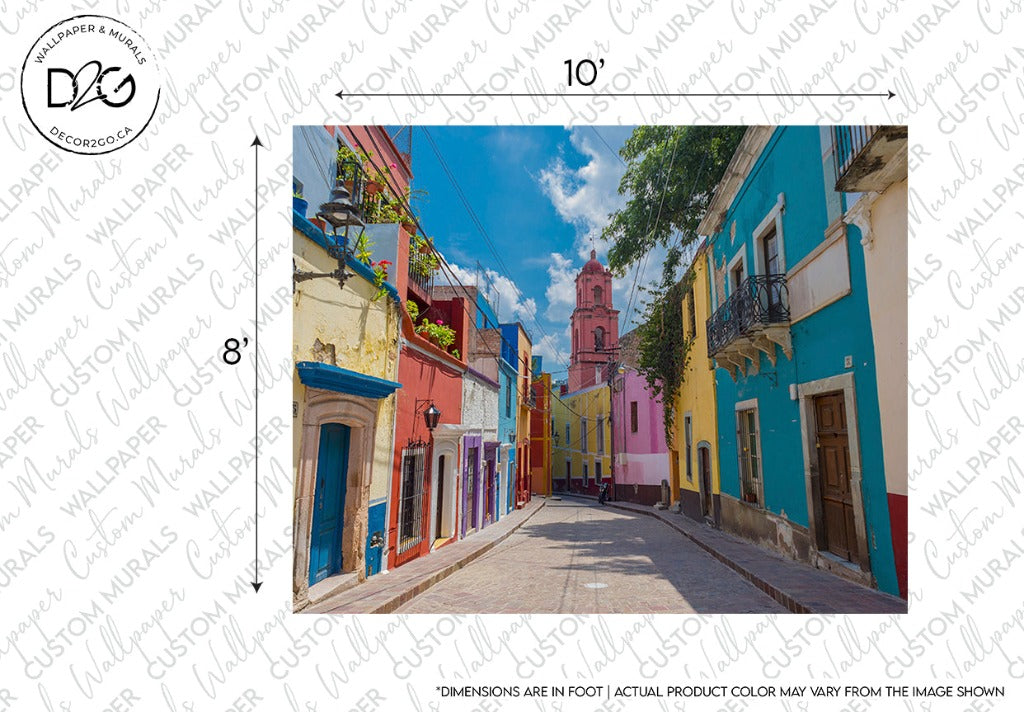 A vibrant colour palette street with houses in shades of blue, yellow, and red leading towards a pink church tower under a clear blue sky indicates the Decor2Go Wallpaper Mural Rainbow Road wallpaper design with dimensions labeled.
