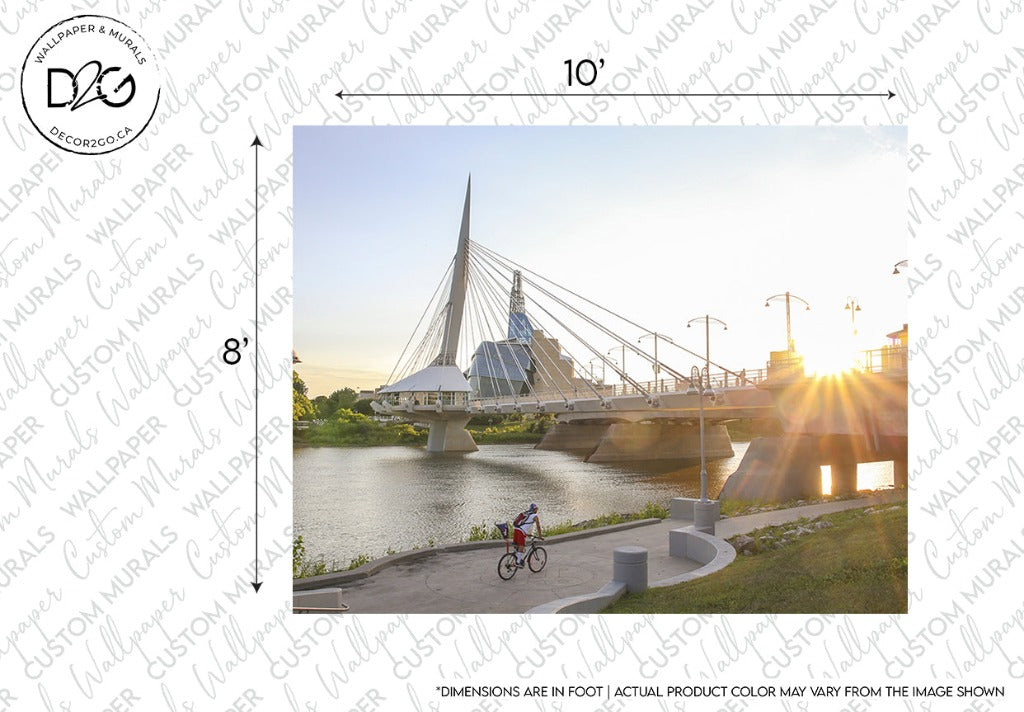 A cyclist rides along a riverside path near the Decor2Go Wallpaper Mural with a tall, white spire and cables at sunset. Soft sunlight illuminates the scene, highlighting the bridge and reflective water.