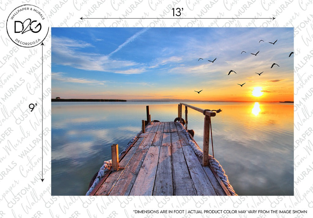 A wooden pier extends into a calm lake during a vibrant sunset. The sky is painted with shades of orange, yellow, and blue, and several birds are flying in the distance. The water reflects the natural beauty and colors of the sky and setting sun on the horizon—a perfect scene for Sunset Birds Flying Wallpaper Mural made with high-quality materials by Decor2Go Wallpaper Mural.