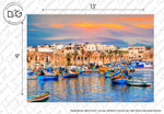 A scenic view of a harbor with colorful traditional Maltese boats (luzzus) floating on blue water, backed by historic beige stone buildings under a sunset sky with pink and orange hues, perfect for the Forever Malta Wallpaper Mural by Decor2Go Wallpaper Mural.