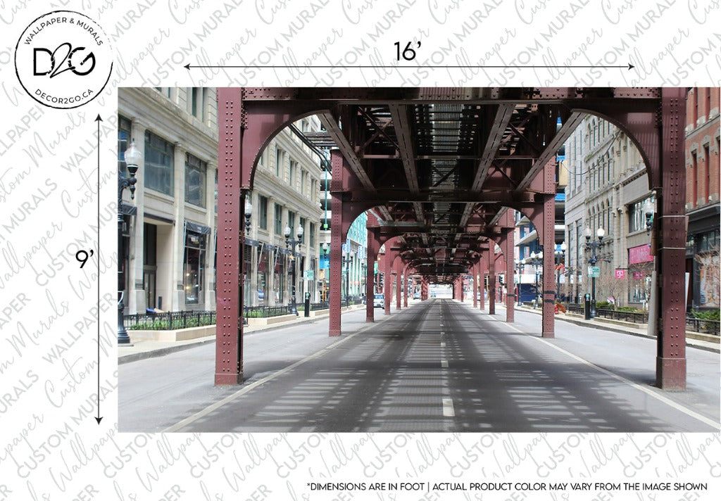 A street with an overhead metal structure, reminiscent of an Urban Railway Wallpaper Mural by Decor2Go Wallpaper Mural, runs through an area featuring historic buildings. The measurements show the structure as 16 feet wide and 9 feet high. Street lamps line the sidewalk, enhancing the urban aesthetic, while the road appears empty.