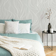 Bedroom - A cozy bedroom corner featuring a bed with turquoise blankets, a white knitted throw, and a decorative pillow, beside a small round table with a vase and candles, against a Decor2Go Leafy Waves Wallpaper Mural.