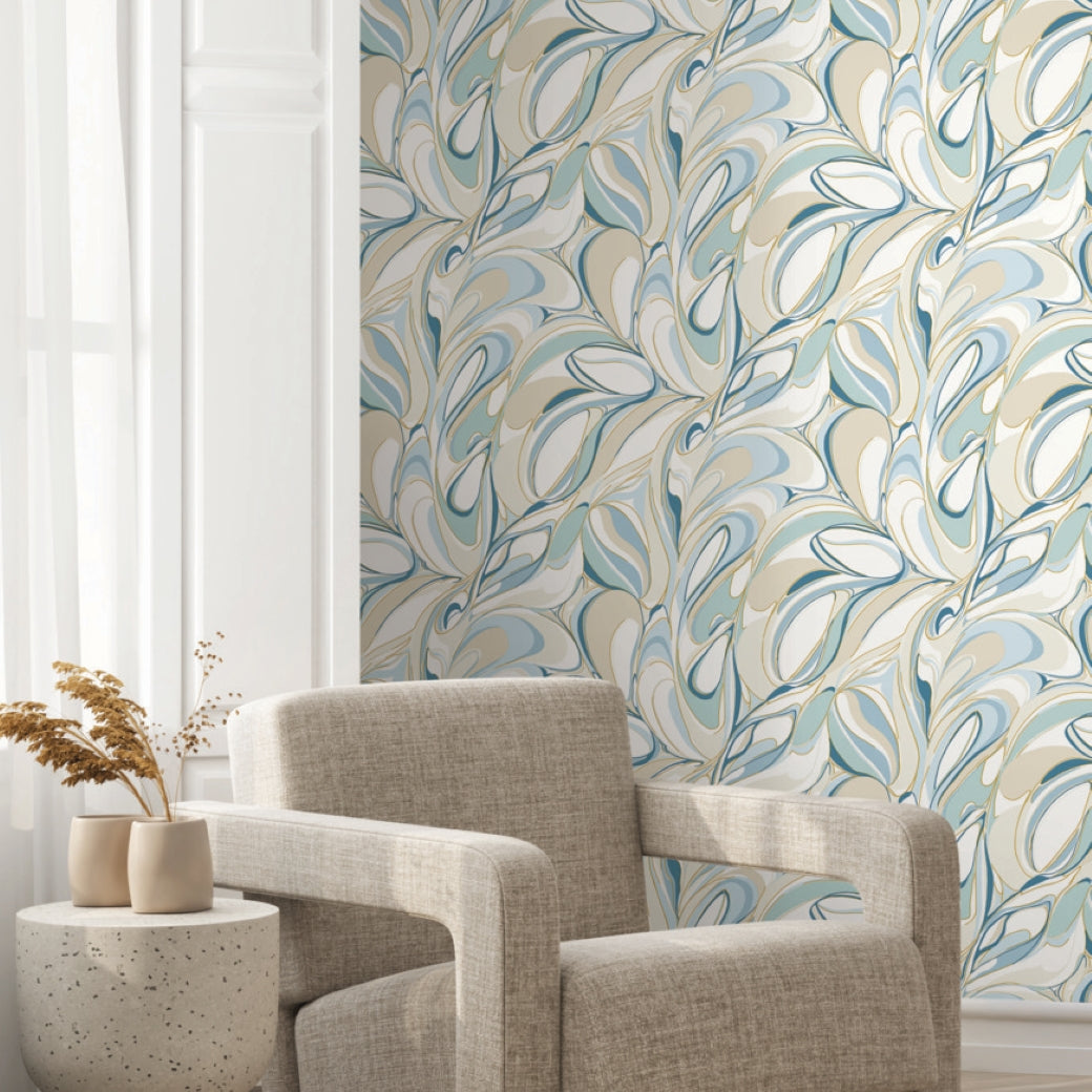 A cozy beige armchair and a small round table with a vase of dried plants sit before a wall adorned with York Wallcoverings' Achate Blue Wallpaper (60 SqFt) featuring blue, green, and cream tones.