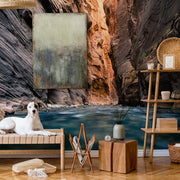 Living Room - A serene living room setup featuring a white dog lying on a futon, surrounded by a shelf, wicker ornaments, and a wooden table, all set against the Decor2Go Wallpaper Mural of Adventure Canyon.