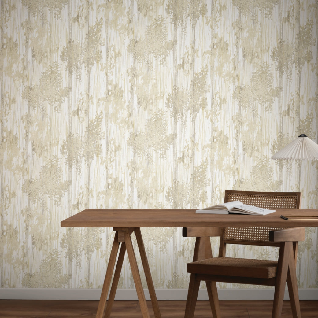 A wooden desk with an open book, a woven-back chair, and a table lamp sits in front of beige and white Aspen Grove Sand Wallpaper (60 SqFt) by York Wallcoverings, featuring an abstract leafy pattern.