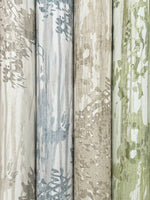 Four rolls of York Wallcoverings Aspen Grove Blue Wallpaper (60 SqFt) stand vertically side by side, featuring abstract, nature-inspired patterns in muted blue, beige, gray, and green for a subtle watercolor botanical look.