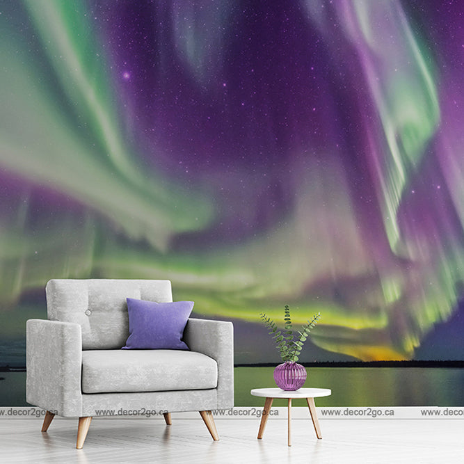 A modern living room with a gray armchair and a small round table featuring a plant and a purple cushion, set against a Decor2Go Wallpaper Mural of the Aurora borealis.