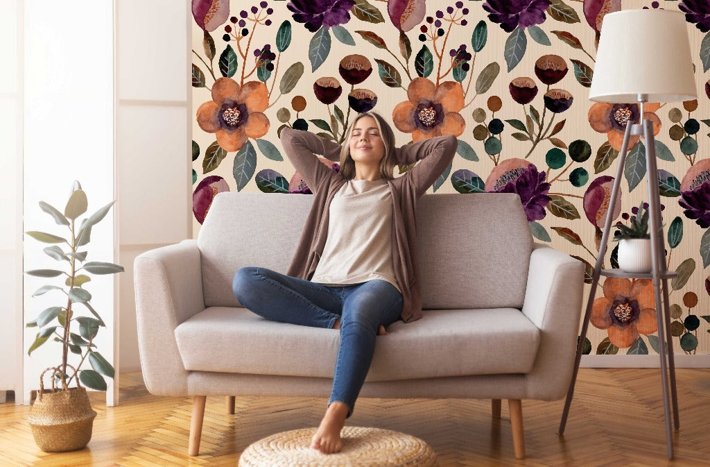 A woman relaxes on a sofa with arms outstretched, legs crossed, in a cozy living room with Decor2Go Wallpaper Mural floral oil paint wallpaper and tasteful decor, including a floor lamp and potted plant.