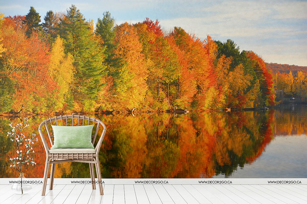 A scenic Fall Foliage Symphony Wallpaper Mural: vibrant, colored trees reflecting in a calm lake, with a white chair in the foreground facing the scene on a wooden deck by Decor2Go Wallpaper Mural.