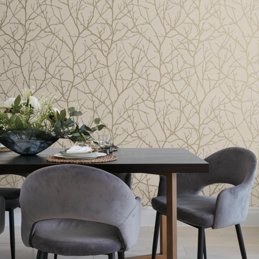 A Modern Metals Collection dining table comes with two gray chairs and a black metal frame, adorned with a floral centerpiece. The background features York Wallcoverings Beige & Gold Trees Silhouette Wallpaper, enhancing the cozy elegance of the setup.