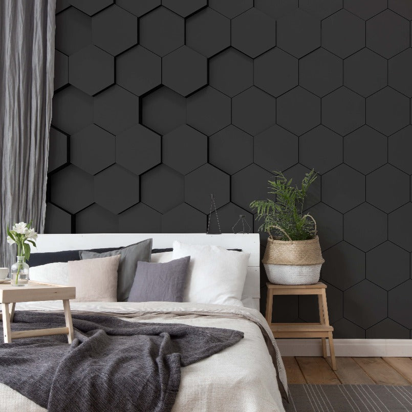 Modern bedroom with a bed covered in neutral-toned linens, a small wooden side table with plants, and a distinctive Decor2Go Black Hexagons 3D Wallpaper Mural. A gray curtain hangs on the