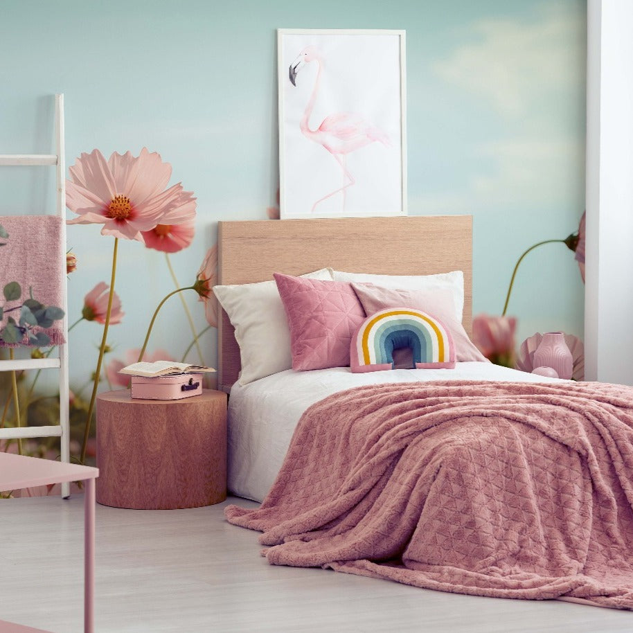 A cozy bedroom with a soft pink and beige color scheme, featuring a bed with a pink quilt, a rainbow-shaped pillow, and vibrant blooms framed as the Decor2Go Wallpaper Mural on the wall.