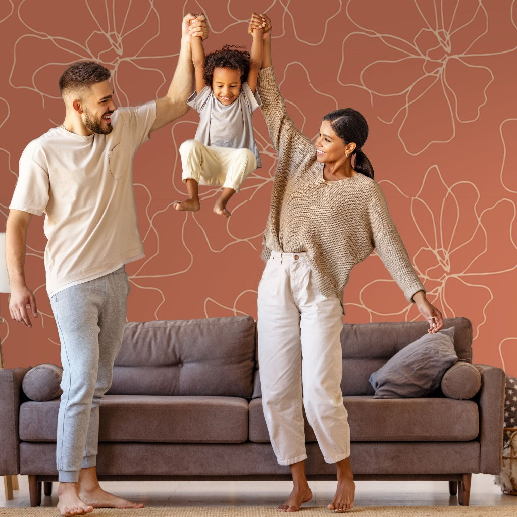 A cheerful family with a man, a woman, and a child are playing together in a living room featuring customizable sizing options and Decor2Go Wallpaper Mural's Blossom Flower Lines Wallpaper Mural in the background. The tranquil atmosphere is highlighted as the man and woman lift the smiling child up by their arms.