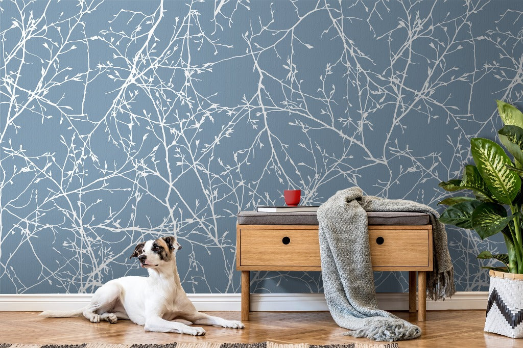 A cozy room featuring a wall adorned with Decor2Go Wallpaper Mural, a wooden side table with a cup and a gray blanket, a large potted plant, and a relaxed white and brown dog lying on the