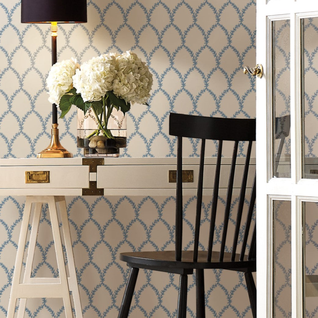 The stylish interior includes a white desk with gold accents featuring a lamp and vase of white flowers. A black chair complements York's Blue/White Laurel Wallpaper (60 SqFt), while an open glass door adds to the room's airy feel.