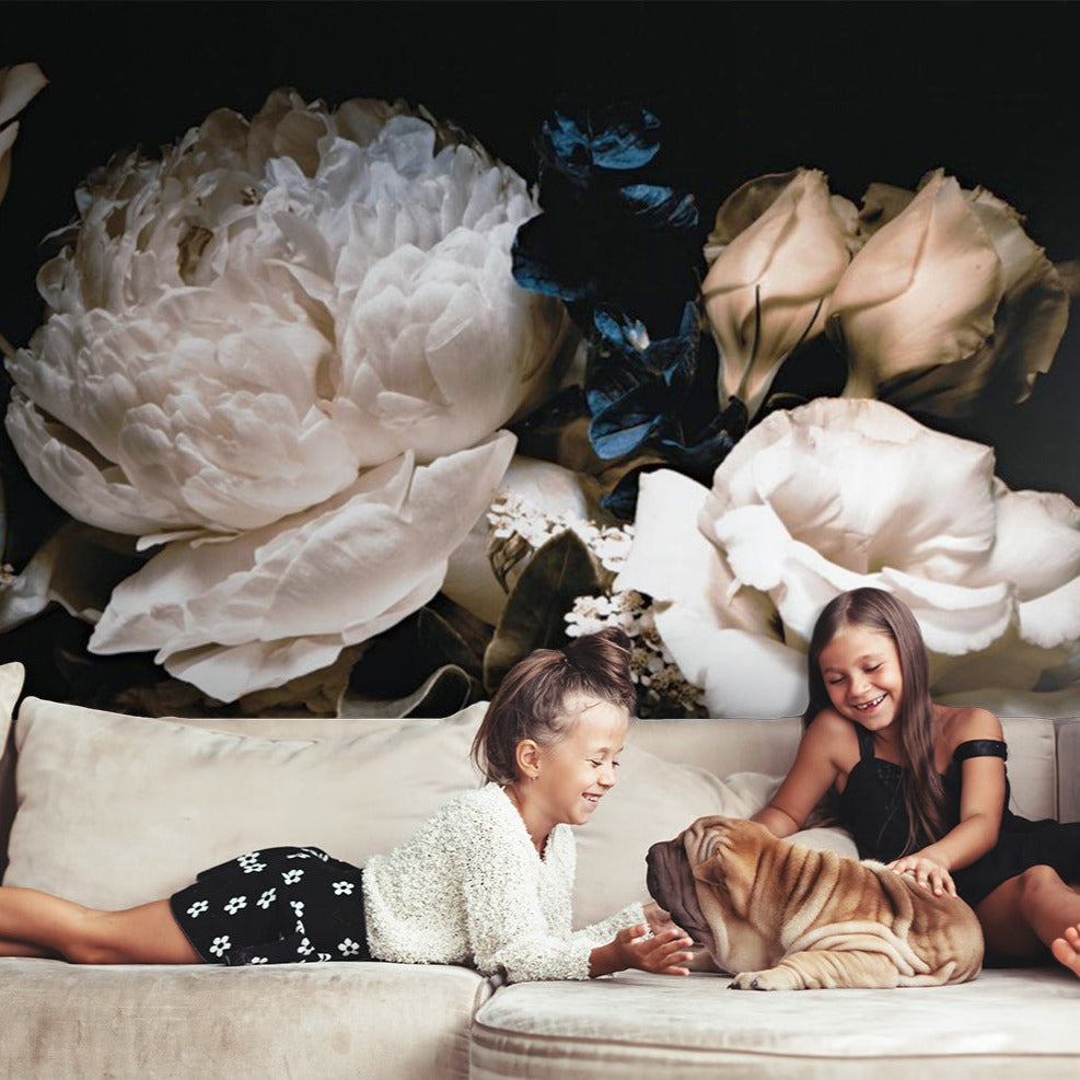 Two joyful young girls and a dog lounging on a sofa, surrounded by oversized delicate Bouquet of White Peonies Wallpaper Mural against a dark backdrop, depicting a serene and playful moment. Brand Name: Decor2Go Wallpaper Mural