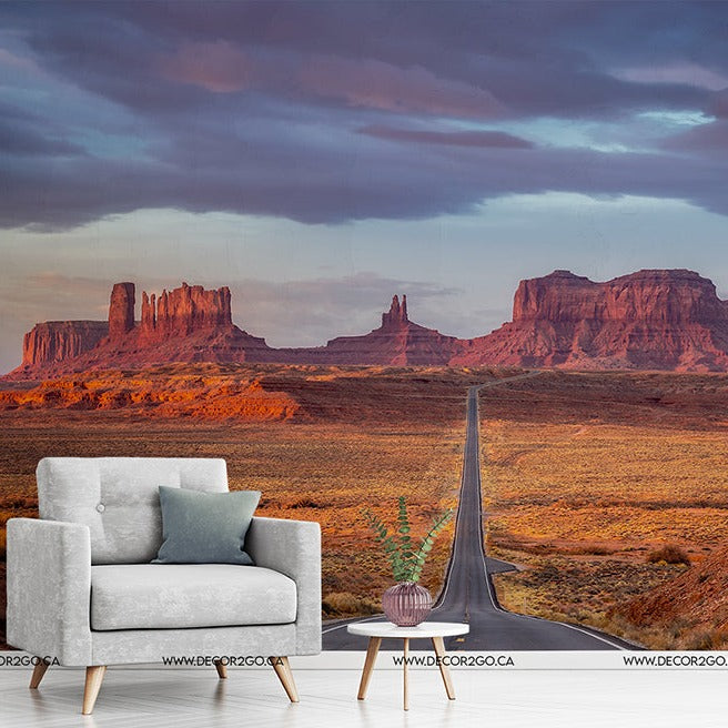 A surreal interior concept with a modern gray armchair and a small table, positioned on a seamless transition to a Decor2Go Wallpaper Mural under a vibrant sunset sky.