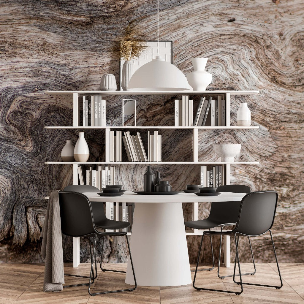 Modern dining room with a white circular table, four gray chairs, and a shelving unit filled with books and decorative items. The room features a striking wall covered with Decor2Go Wallpaper Mural.