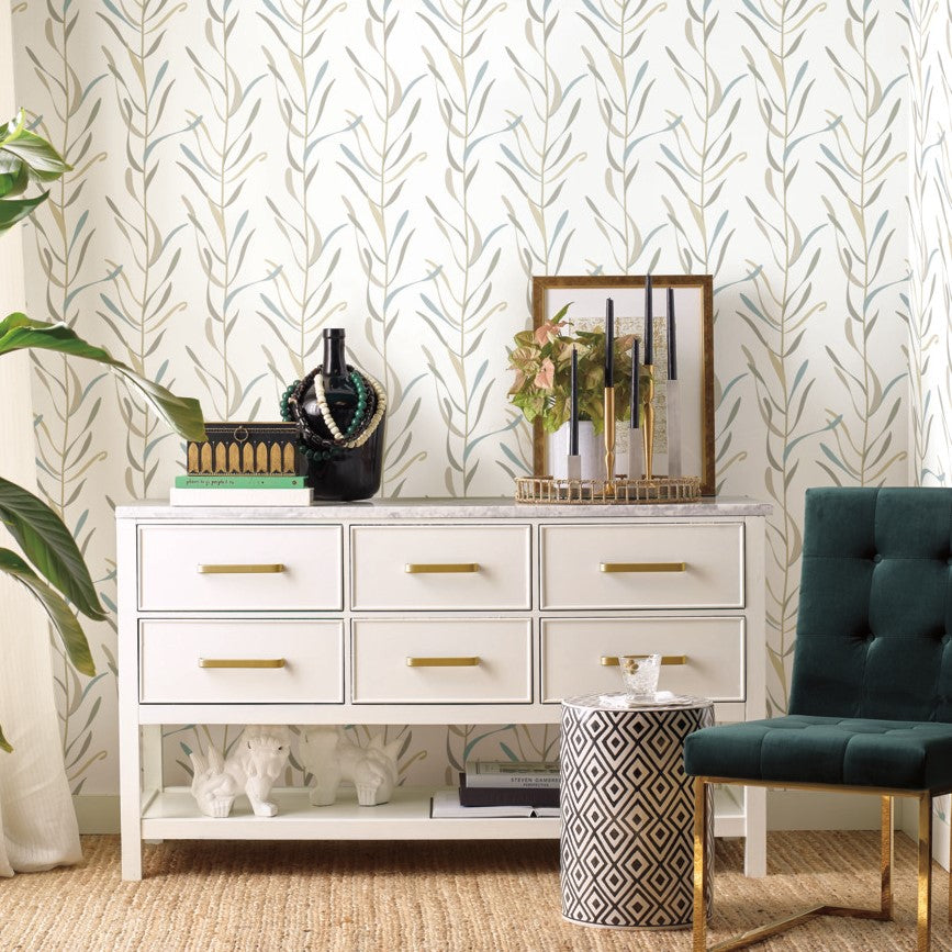 A stylish room with a white dresser displaying decorative items, a green armchair, and a wall covered in York Wallcoverings Chloe Vine River Rock Wallpaper Beige, Grey (60 Sq.Ft.). The setting is elegant and modern.