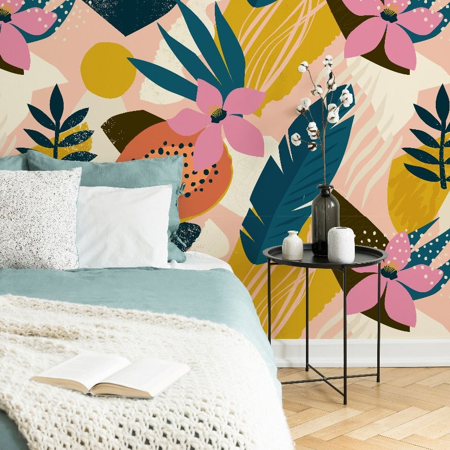 A cozy bedroom featuring a vibrant Collage Contemporary Floral Wallpaper Mural from Decor2Go Wallpaper Mural with large pink and blue flowers, a bed with teal bedding and a white knitted throw, beside a small table with a plant and candles.