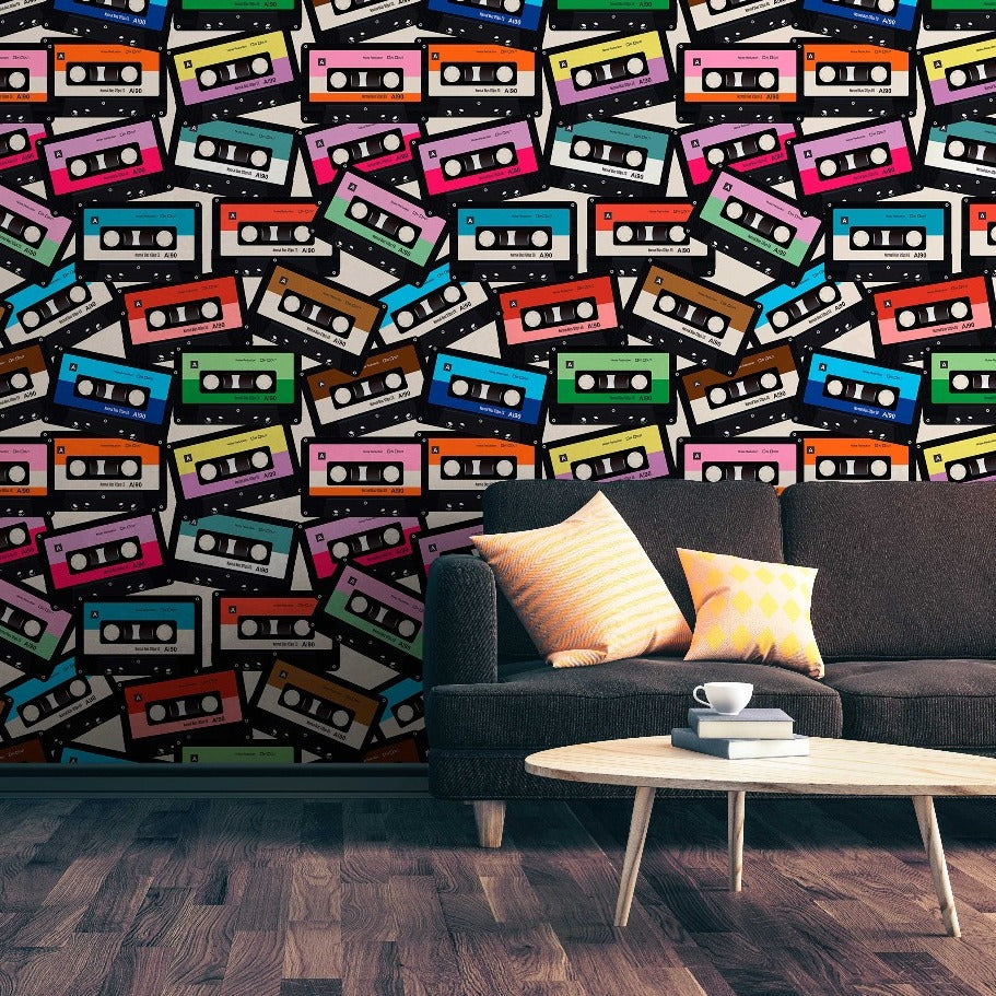 A modern living room with a gray sofa adorned with colorful pillows, in front of a vibrant wall covered in Decor2Go Wallpaper Mural's Coloured Cassette Wallpaper Mural. A white coffee table with a cup on it sits on a wooden floor.