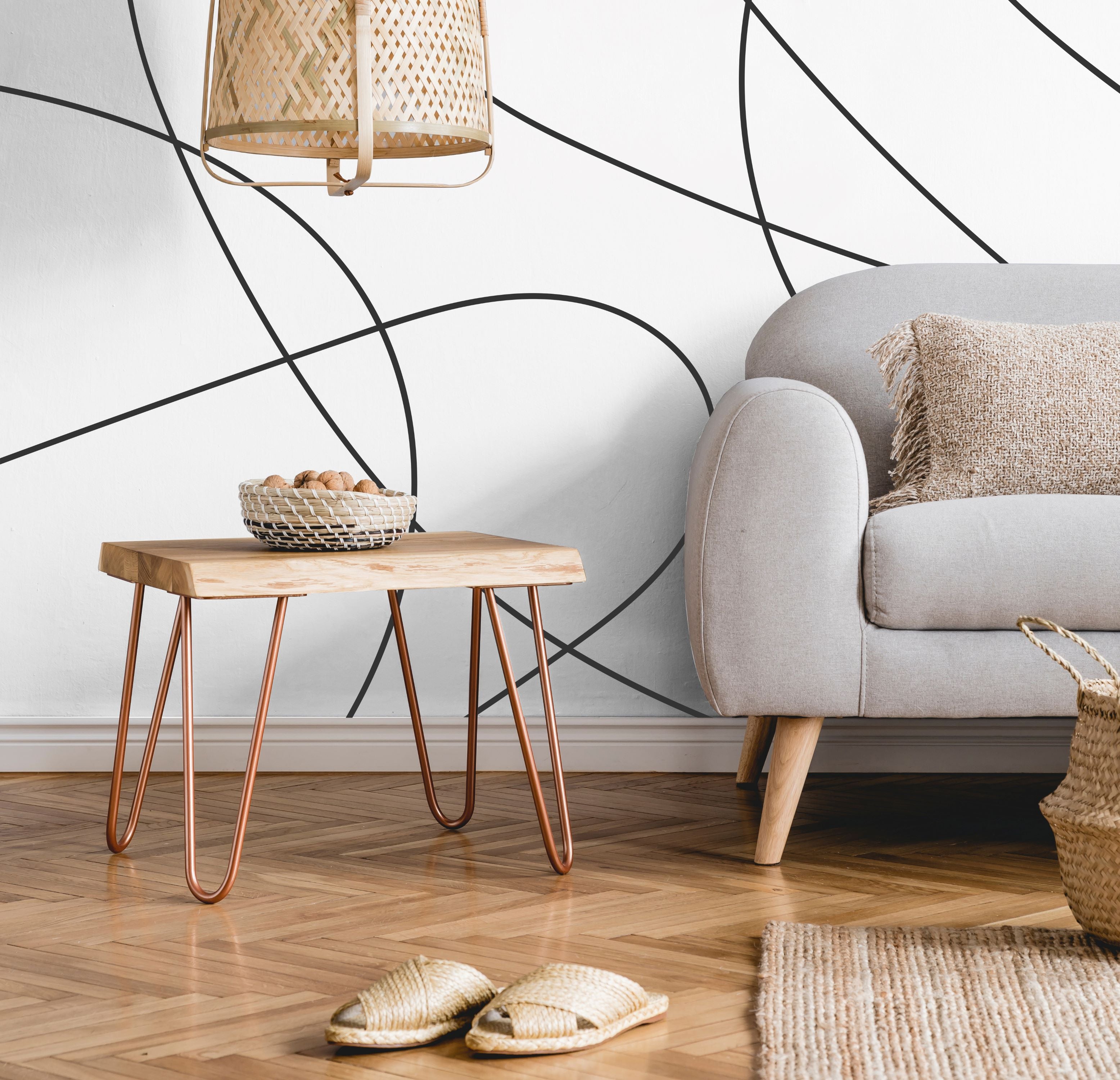 Living Room - A modern living room with a light gray sofa, a wooden side table with copper legs, and a bowl of nuts on the table. A woven lamp hangs above, while a basket sits on the hardwood floor adorned with woven slippers. The walls feature Decor2Go Winnipeg's Contemporary Scribble Elegance Wallpaper Mural that adds an artistic flair to the space.