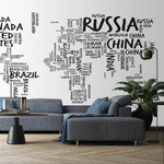 A modern living room with a large Decor2Go Wallpaper Mural Country Names Map on the wall where countries are represented by their names in different font sizes. The room has a blue sofa, a coffee table, and a p