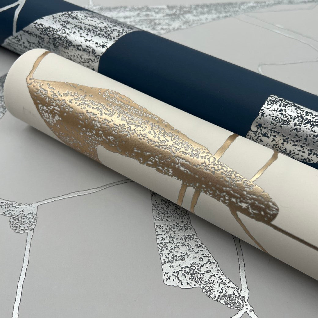 Close-up of two wallpaper rolls: the first in navy with silver and white abstract patterns from the Modern Metals Collection; the second, York Wallcoverings' Warm Grey & Gold Harlowe Wallpaper, features light grey with vintage gold and silver accents on a matching surface.