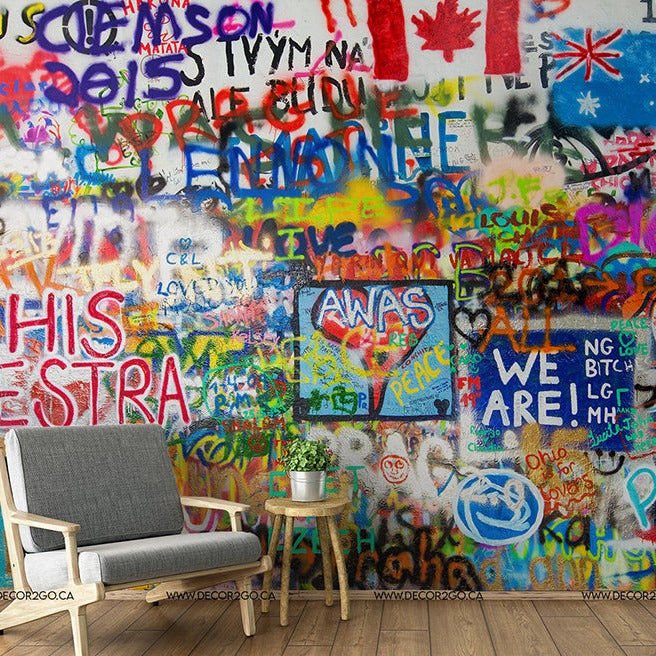 A vibrant Creative Freedom Wallpaper Mural with various colors and symbols, including flags and text, in a room beside a white chair with a small round table and decorative items from Decor2Go Wallpaper Mural.