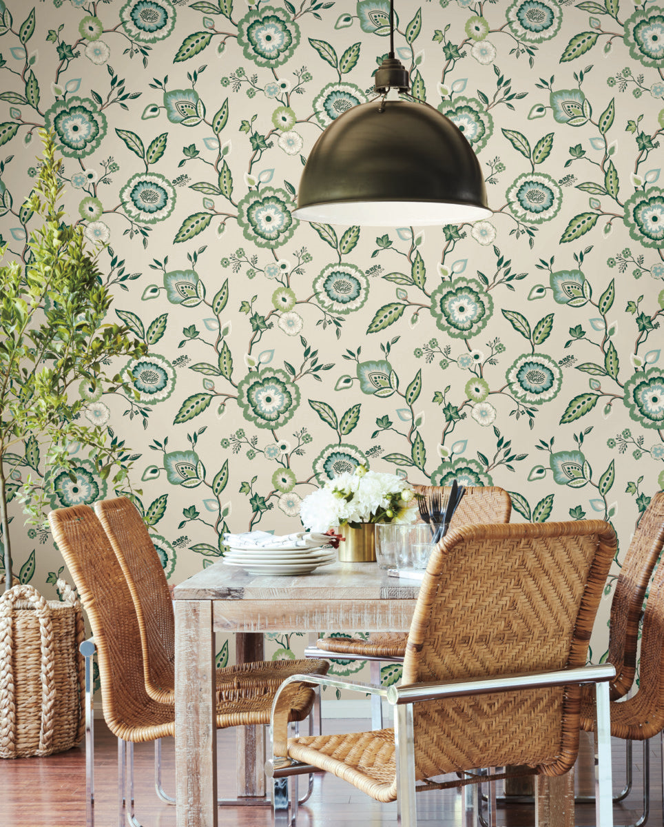 A dining area featuring a wooden table surrounded by wicker chairs with metal frames. A metallic dome-shaped pendant light hangs above the table, which is adorned with white flowers. The background wall showcases botanical elegance with **York Wallcoverings** Dahlia Blooms Midnight/Multi Wallpaper Black, Pink (60 Sq.Ft.) that's easy to install and remove.