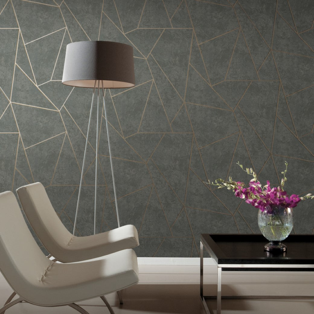 A modern living room showcases two white chairs, a tall floor lamp, and a black side table with a vase of purple flowers. The wall features York Wallcoverings' Dark Grey & Gold Nazca Wallpaper, bringing muted metallic elegance to the space.