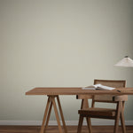 A minimal desk scene featuring a wooden table, open book, wooden chair with woven back, and modern white lamp, set against York Wallcoverings Dew Drop Grey Wallpaper (60 SqFt) for a subtle touch of color.