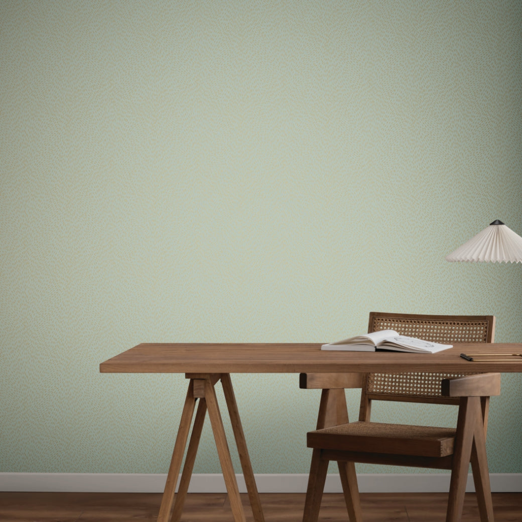 A minimalist workspace features a wooden desk and chair, an open book, and a hanging lamp set against York Wallcoverings’ Dew Drop Sea Mist Wallpaper (60 SqFt), creating a serene scene with natural tones and clean lines.