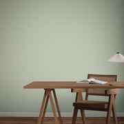 Home Office - A minimalist features a wooden desk and chair, an open book, and a hanging lamp set against York Wallcoverings’ Dew Drop Sea Mist Wallpaper (60 SqFt), creating a serene scene with natural tones and clean lines