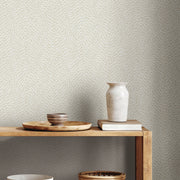 A wooden shelf displays a round tray with two ceramic bowls and a white vase on stacked books, set against light walls covered in York Wallcoverings' Dew Drop White Wallpaper (60 SqFt) with a subtle dotted pattern.