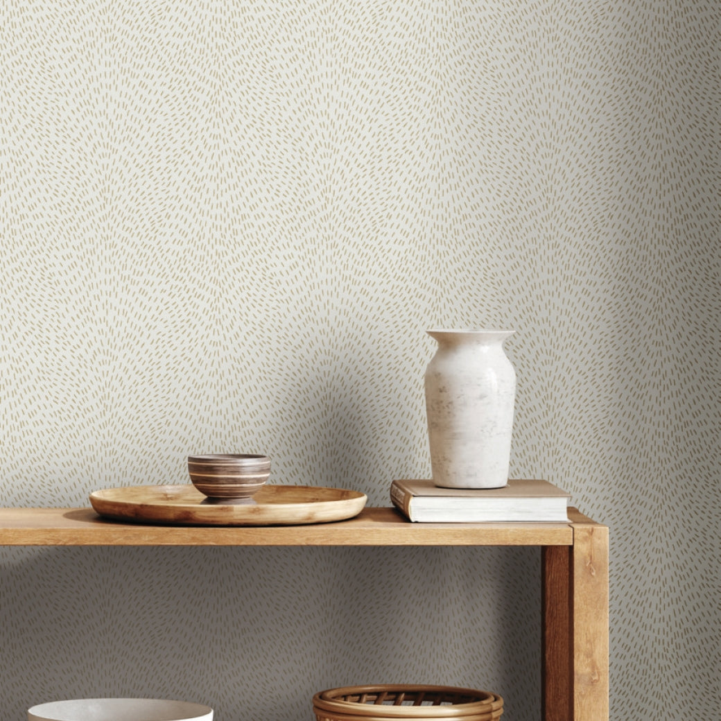 A wooden shelf displays a round tray with two ceramic bowls and a white vase on stacked books, set against light walls covered in York Wallcoverings' Dew Drop White Wallpaper (60 SqFt) with a subtle dotted pattern.
