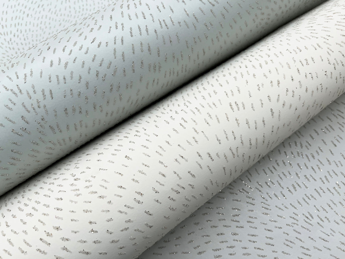 Close-up of two rolls of York Wallcoverings Dew Drop Beige Wallpaper (60 SqFt), featuring light gray and off-white tones with subtle scattered silver dashes that add a hint of shimmer and elegant glitter effect to your space.