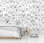 A modern bedroom with a Decor2Go Wallpaper Mural featuring various cartoon dog faces in black and white. The room has a bed with gray bedding, a small wooden bedside table, and a floor cushion.