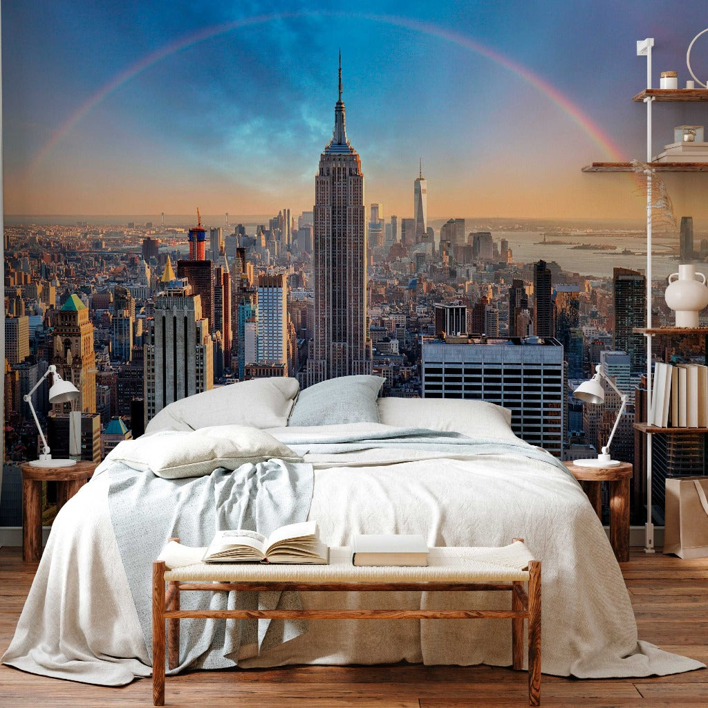 A bedroom with a large bed, book on the bench at its foot, and a Decor2Go Wallpaper Mural of New York City showcasing the stunning Double Rainbow Skyline over the skyline.