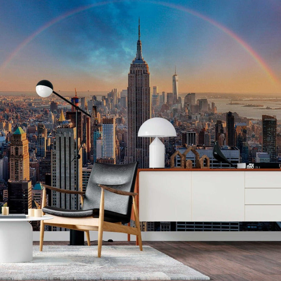 A modern living room with stylish furniture overlooking a cityscape with the Empire State Building and a Decor2Go Wallpaper Mural Double Rainbow Skyline in the sky at sunset.