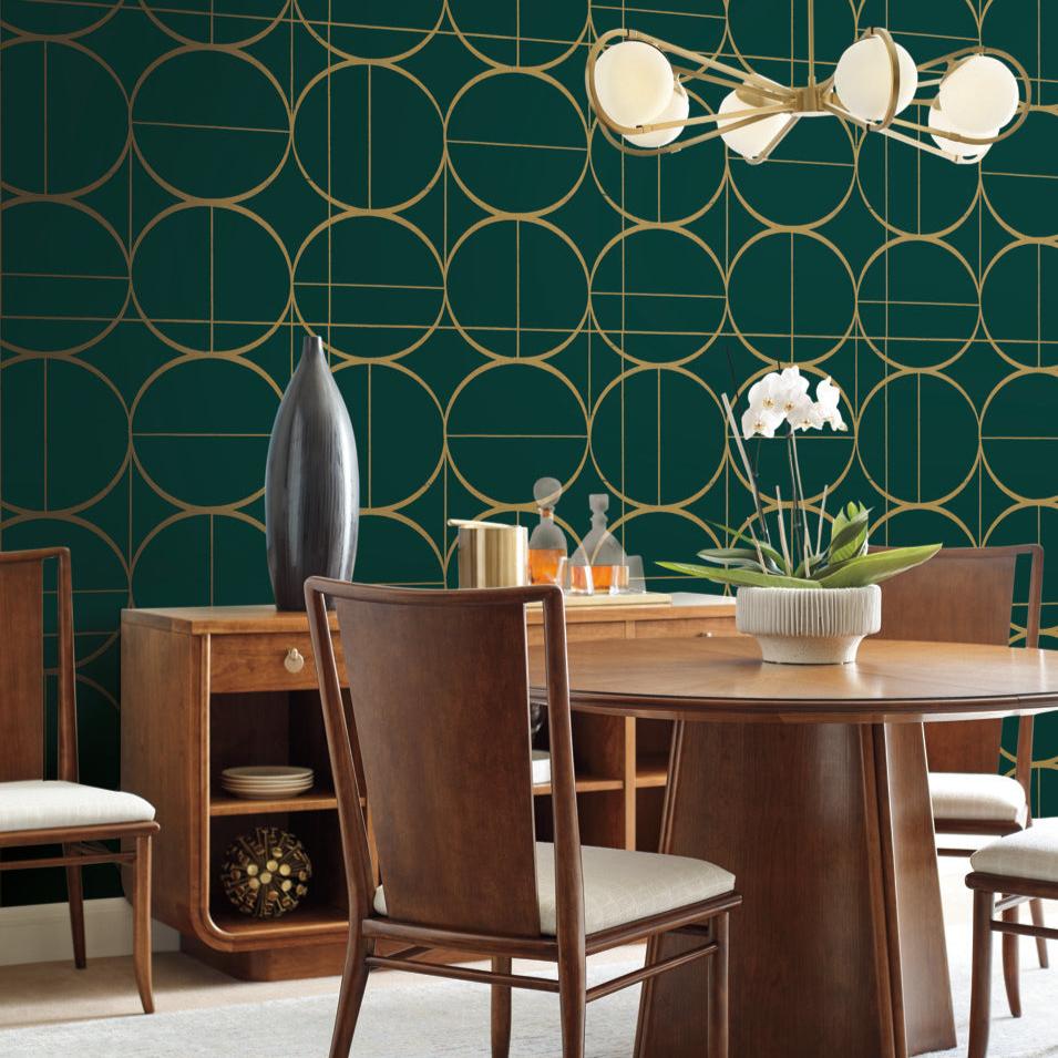 Elegant dining room with wooden furniture and a round table, highlighted by York Wallcoverings' Emerald & Gold Sun Circles Wallpaper. A modern chandelier with metallic finishes hangs above, and the sideboard showcases decorative vases along with an orchid plant.