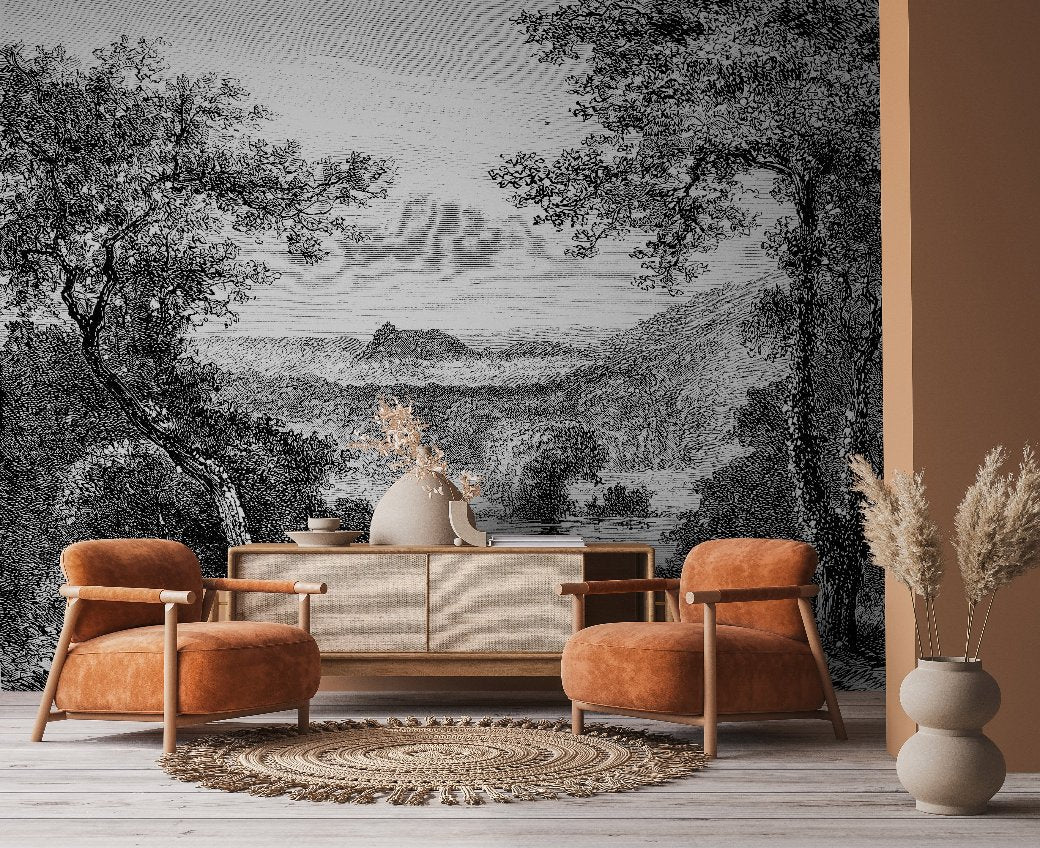 A cozy living room features two burnt orange armchairs, a woven rug, and a sideboard with a vase of dried flowers. The backdrop is Decor2Go Winnipeg's Enchanted Grove Wallpaper Mural, depicting a lush landscape with trees and mountains that creates natural tranquility.