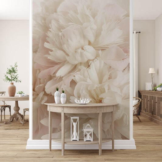 A room adorned with the Whispers of Peonies Wallpaper Mural by Decor2Go features a large-scale design of white peonies. In the foreground, a round wooden table decorated with vases and decorative items enhances the space, while a dining area can be seen in the background, creating a warm and cozy atmosphere.