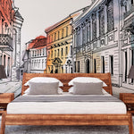 A modern bedroom with a large bed featuring crisp white linens and wooden frame, flanked by matching nightstands with lamps, set against a vibrant Decor2Go Wallpaper Mural of a charming city European Alley Watercolor Wallpaper Mural.
