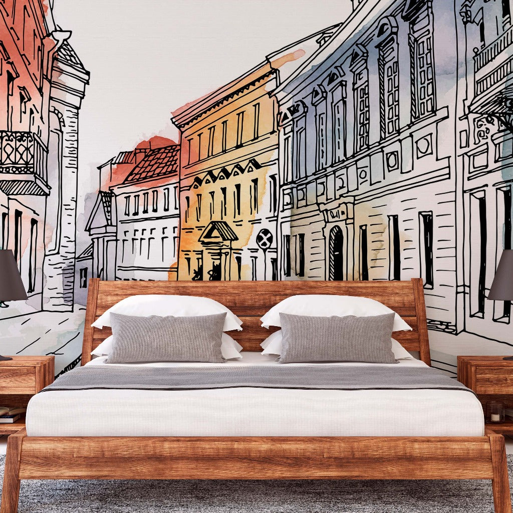 A modern bedroom with a large bed featuring crisp white linens and wooden frame, flanked by matching nightstands with lamps, set against a vibrant Decor2Go Wallpaper Mural of a charming city European Alley Watercolor Wallpaper Mural.