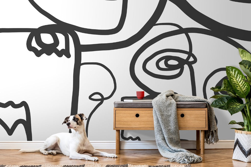 A stylish room featuring a large Face Art Wallpaper Mural from Decor2Go Wallpaper Mural on the wall, a wooden console table with a red mug atop, a draped grey blanket, and a plant. A white and brown dog lounges on